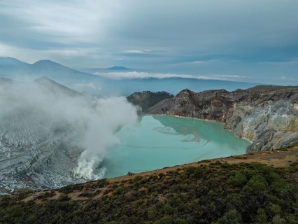 Drone view of Ijen crater in Indonesia with turquoise acidic lake and visible sulfur smoke near the