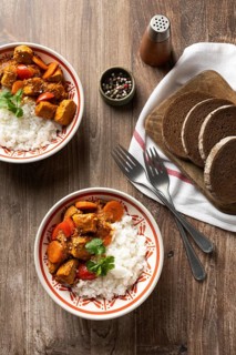 Top view of a bowl of Hungarian pork goulash served with white rice, garnished with a sprig of