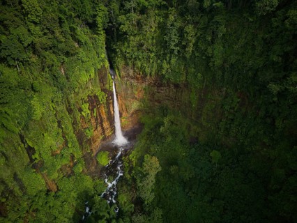 Aerial shot capturing the majestic Kaspa Biru Waterfall descending into a natural gorge, surrounded