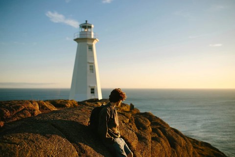 Side view of unrecognizable young man sitting on rocks gazing at the ocean near Cape Spear