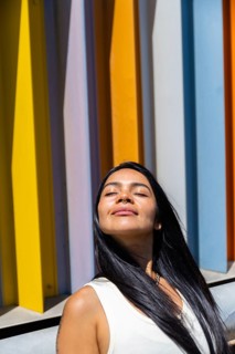 A woman in a colorful outfit enjoys the sunlight, standing in front of a backdrop of vibrant,