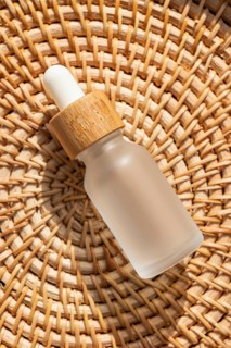 A cosmetic with a wooden cap is placed on a woven rattan mat. The warm lighting emphasizes the