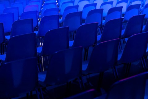 A series of empty blue chairs are arranged in neat rows under a dramatic blue spotlight at a