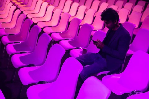 Indian man at a conference of AI in Amsterdam sits amid rows of vibrant purple lit chairs, deeply