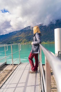 Woman in casual clothes leaning on the railing of a jetty with a view of the lake and mountains,