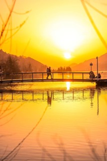 People on a bridge over a lake at sunset with intensive reflection, Großer Alpsee, Immenstadt im