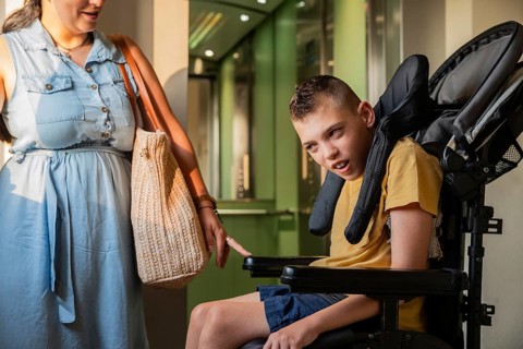 A mother lovingly supports her son with cerebral palsy in a wheelchair. Sunlight highlights their