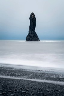 A dramatic sea stack rises from the ocean at Reynisfjara Beach in Iceland, surrounded by mist and