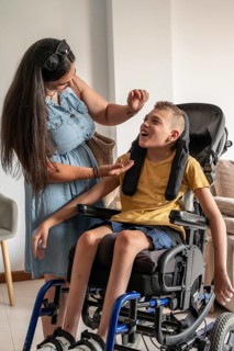 A mother lovingly cares for her son, who has cerebral palsy, sitting in a wheelchair. The scene