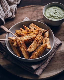 A bowl of rustic potato wedges seasoned with herbs and spices, served with a creamy dip. The