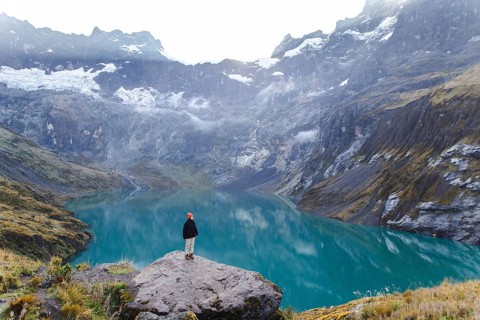 A woman stands on a rocky ledge, overlooking the stunning turquoise lake and surrounding peaks of
