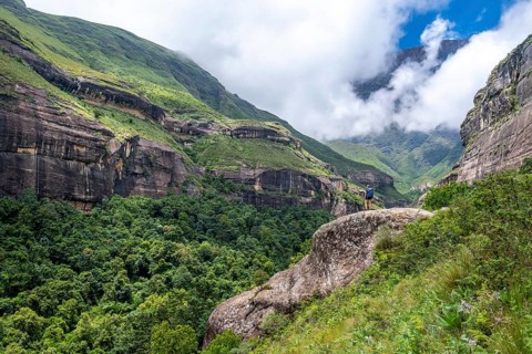 Female hiker standing in front of landscape with mountains and fog, Drakensberg National Park,