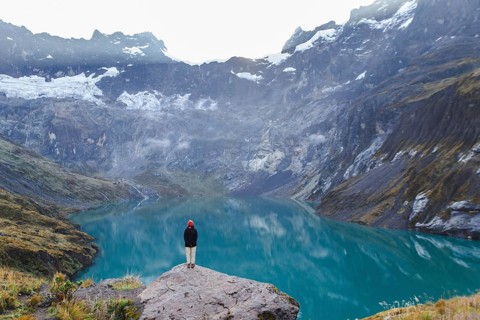 An Ecuadorian woman stands on a rocky ledge, overlooking the serene turquoise waters and majestic