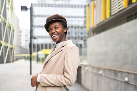 A stylish black woman smiles confidently while standing in a modern urban environment Her chic