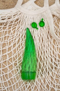 Top view of a green aloe vera gel tube and two green capsules placed on a white net bag, set