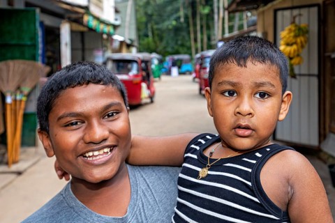 Two young boys pose happily on a street, one smiling, the other seriously, A family in Ratnapura in