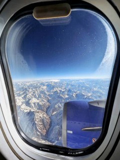 Stunning aerial view of a vast snow-covered mountain range as seen through an airplane window. The