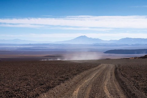 A dusty, gravel road cuts through the arid landscape of La Puna in Argentina, offering a view of