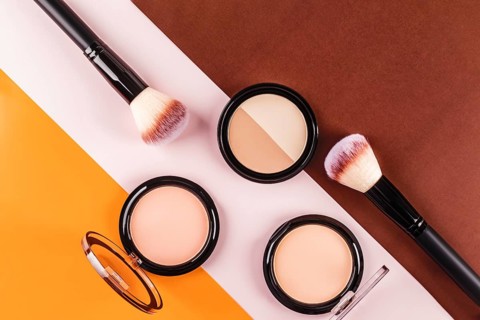 Flat lay of makeup brushes and face powders on a vibrant tricolor background. The contrasting