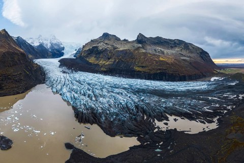 A panoramic shot of the vast Vatnajökull Glacier flowing between rugged mountains under a cloudy