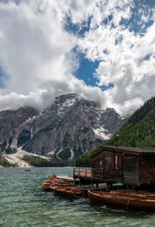 Traditional wooden rowboats rest near a rustic wooden boathouse on Lago di Braies, surrounded by