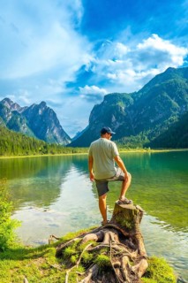 Tourist standing on a tree stump admires the breathtaking landscape of lake dobbiaco, surrounded by