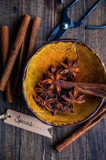Top view of a rustic yellow bowl filled with star anise and cinnamon sticks, accompanied by a pair