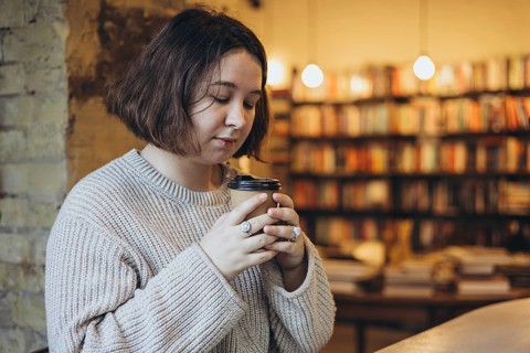 A woman in a soft sweater holds a takeaway coffee cup while enjoying a peaceful moment in a cozy