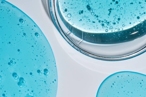 A close-up image of vibrant blue cosmetic gel droplets with visible texture and bubbles, set