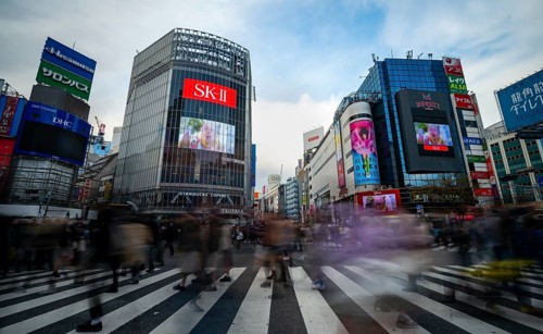 Crowd crossing zebra crossing on a large intersection, motion blur, back modern houses with