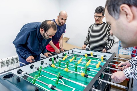 A group of people enjoy a friendly game of foosball at a mental health residence. The activity