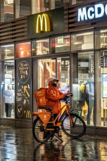 Street at the main station, Lieferando courier, cyclist, rainy weather, city centre, in the