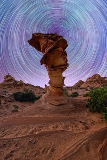 A mesmerizing view of swirling star trails in the night sky above a unique rock formation in a
