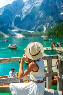 Tourist wearing summer hat looking at lake braies, also called pragser wildsee, with boats and