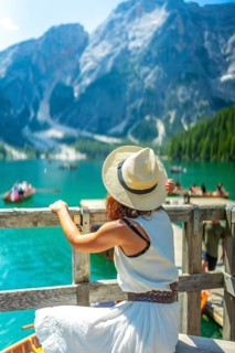 Woman wearing straw hat admiring scenic landscape of lake braies with boats and turquoise water in