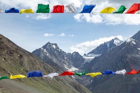 Colorful prayer flags flutter in the foreground, set against the breathtaking backdrop of the