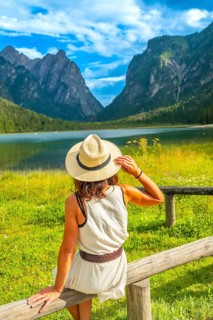 Woman wearing straw hat admiring lake dobbiaco with the dolomites in the background on a sunny