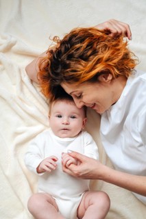 A mother shares a tender moment with her newborn baby girl, lying on a soft, cream-colored blanket.