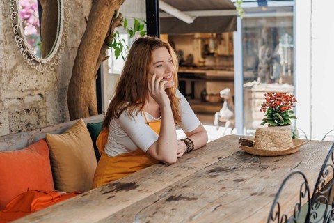 A mature woman, wearing an orange and yellow outfit, enjoys a phone call during her vacation in an