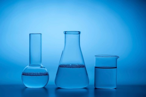 Glass laboratory beakers and flasks filled with water against a serene blue background,