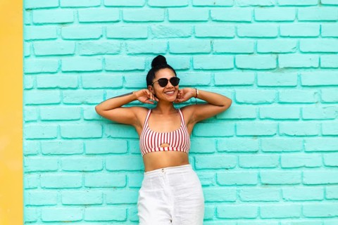 A young Latin woman stands against a vibrant turquoise wall in Mancora, Peru. Wearing a striped top