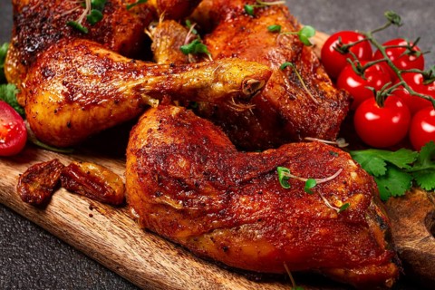 Grilled fried chicken legs, served with fresh cherry tomatoes, and herbs, on a wooden chopping