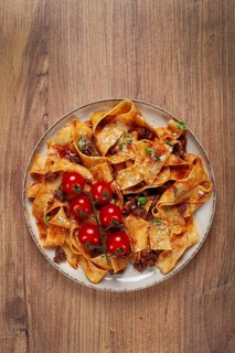 Pappardelle pasta with bolognese sauce, topped with parmesan cheese and cherry branch, homemade, no