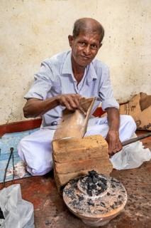 Elderly man works with bricks and coal in traditional clothes, a man burns sapphires in a small