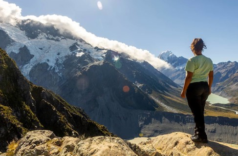 A woman enjoys the stunning autumn view of Mount Cook, New Zealand, standing on a rocky vantage