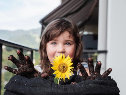 A smiling young girl shows off a bright sunflower and her dirty hands after gardening, capturing a