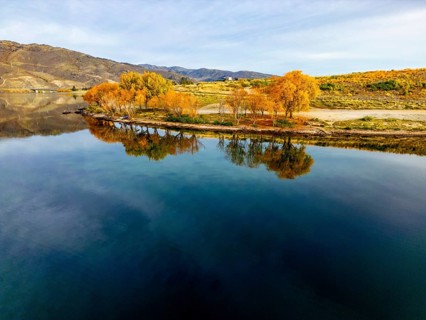 Aerial view of a tranquil lake in Queenstown during autumn, showcasing vibrant foliage and clear