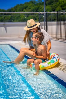 Vertical photo full length of a caucasian mother and kid playing sitting on a swimming pool