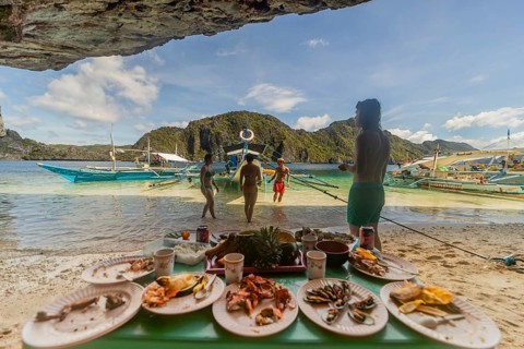 Unrecognizable tourists enjoy a seaside meal in the Philippines, showcasing a vibrant beach