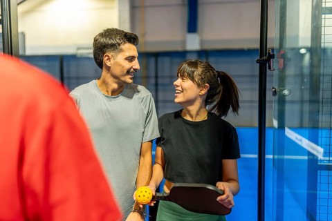 Two smiling adult players holding a paddle and ball, sharing a moment during a friendly pickleball